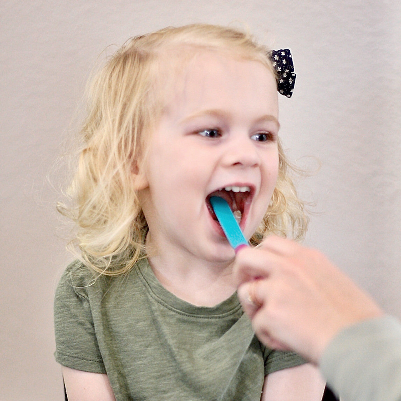 Child opening mouth with the tongue depressor placed on tongue by adult.