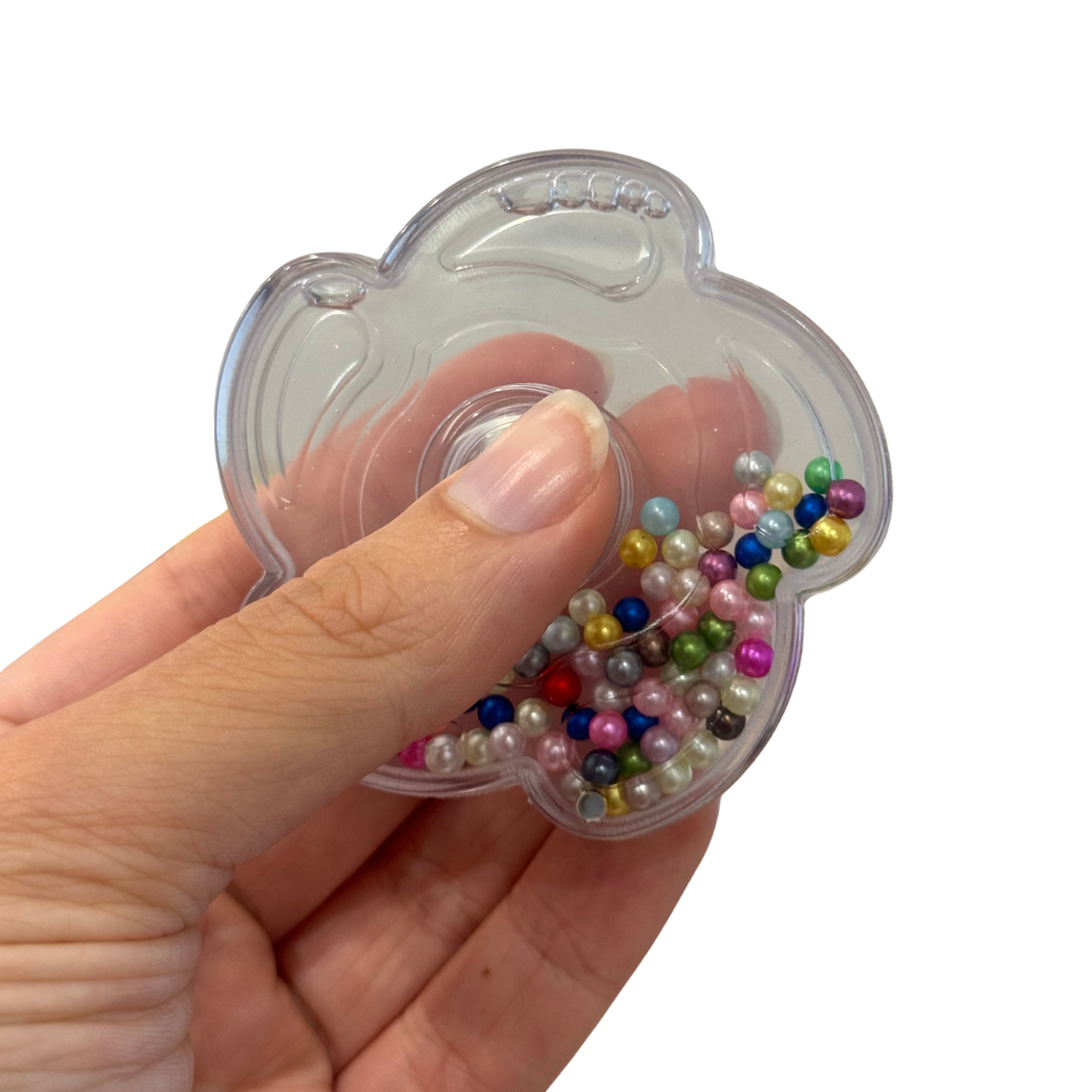Hand holding a clear fidget spinner filled with multicolored beads on a white background