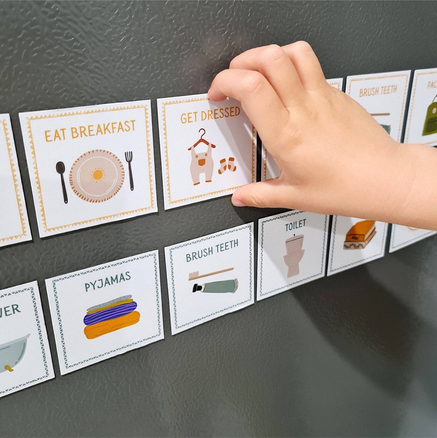 Child's hand interacting with routine magnetic cards on a dark fridge surface