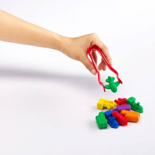 Hand using red jumbo tweezers to pick up a small green airplane on a white background