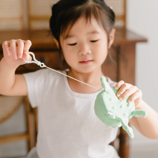 A young girl pulling the white drawcord of the green turtle vibrating handheld Senseez attachable pal.