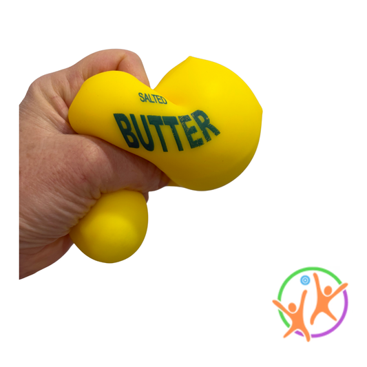 A hand squeezing a bright yellow squishy butter toy shaped like a butter bulb with the words 'SALTED BUTTER' printed