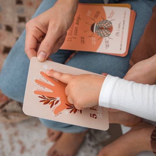 Hand holding a small card with an illustrated hand for 5 finger breathing and a child tracing the fingers.