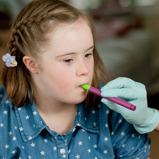 gloved hand assisting a young girl using the bite n chew tip for the z vibe to assist with lip closure. Girl has braided hair wearing a blue shirt with star patterns.