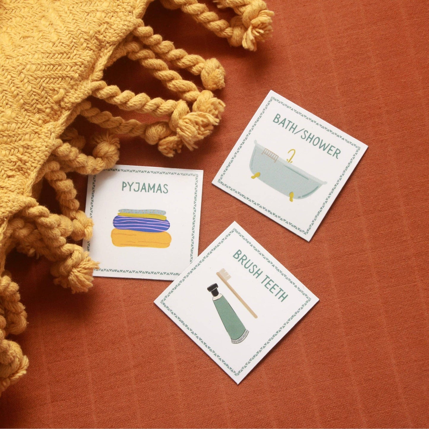 Three magnetic cards about bedtime routine of brush teeth, bath and pyjamas, on a textured surface with a yellow blanket.