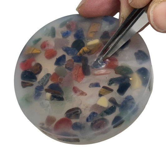 Round Kaiko Pick em pad with colourful embedded stones getting picked out by a hand held tweezer