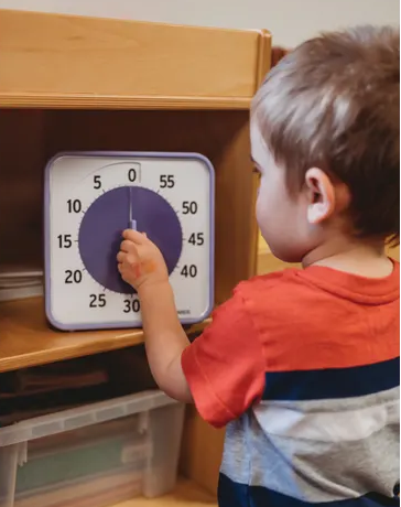 Child interacting with a large 8 inch square visual time timer on a wooden shelf