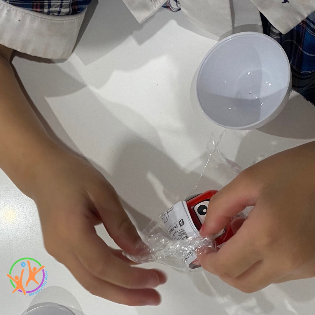 Hands unwrapping a small red and white package on a white surface