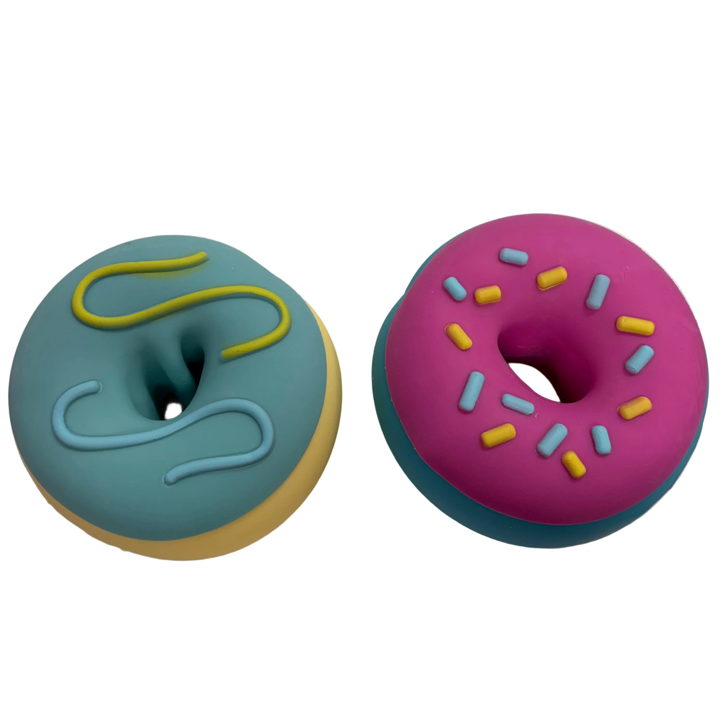 Two donut-shaped  Big Squish squishy toys on a white surface. One donut has a teal frosting top with yellow and light blue swirls, and the other has a pink frosting top with yellow and light blue sprinkles.