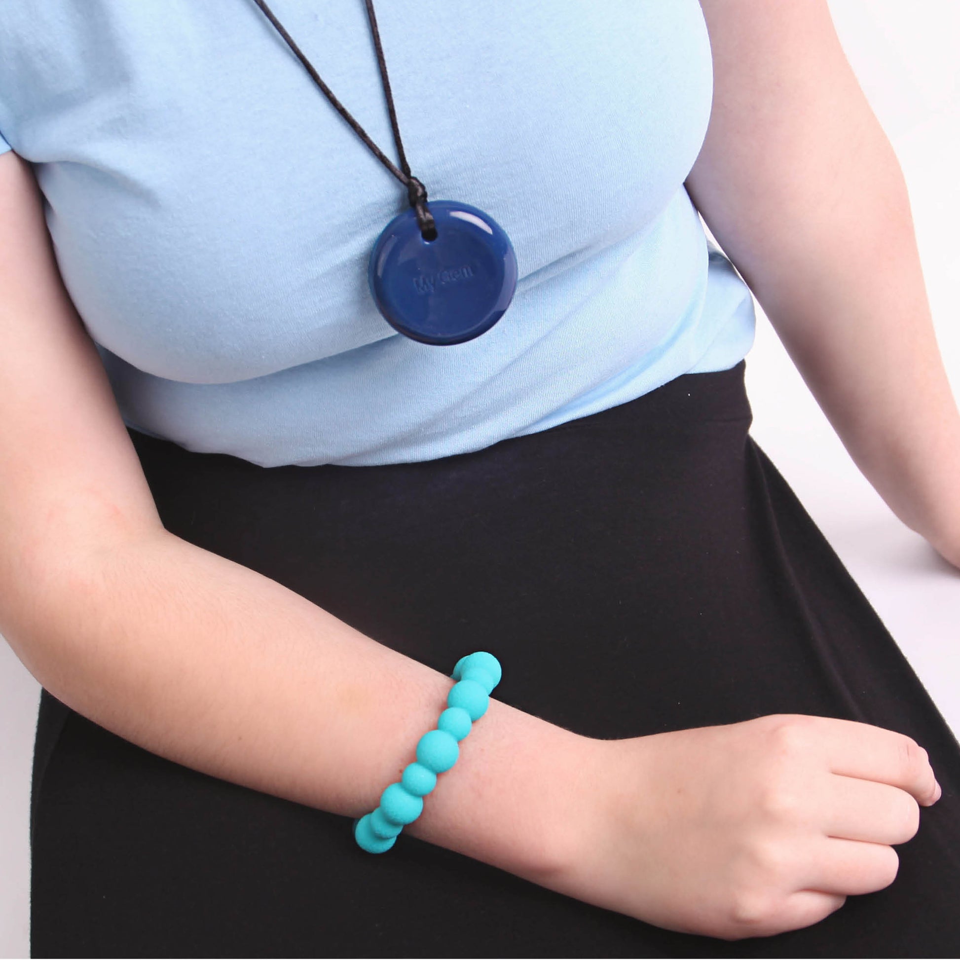 Person wearing a chewigem blue button chew pendant necklace and turquoise bracelet on a plain background