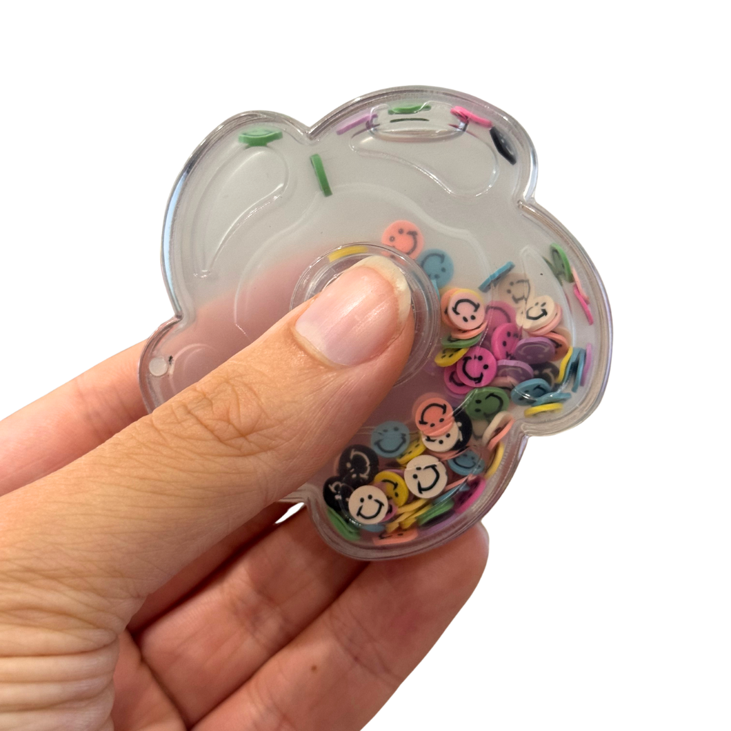 Hand holding a clear fidget spinner with colorful smiley face beads on a white background