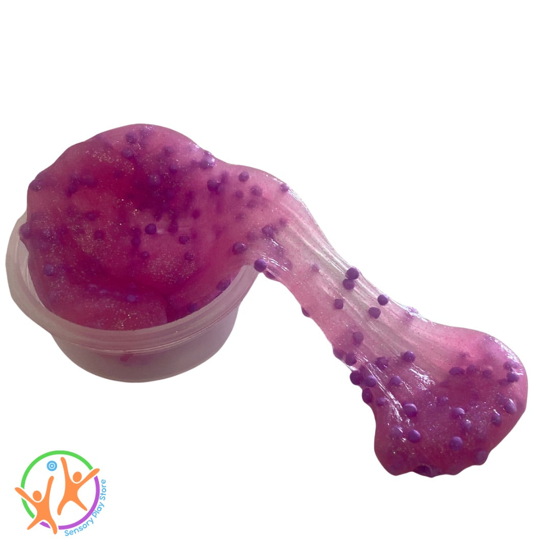 Pink glitter crunchy putty with small beads in a clear container on a white background