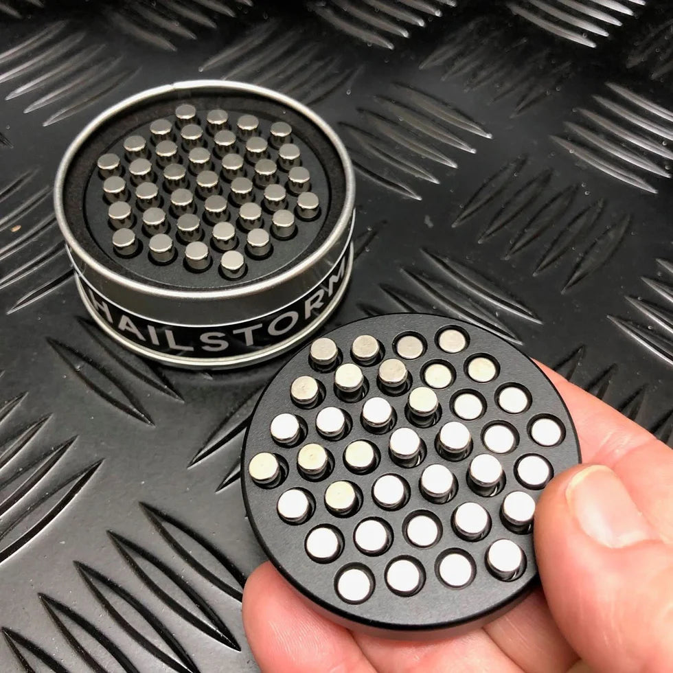 Round metal disc with pins called kaiko hailstorm in hand and in a tin