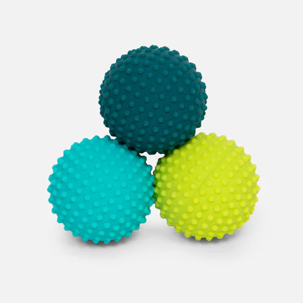 Three textured speks dots silicone massage balls in teal, blue, and lime green stacked to form a triangle on a light gray background
