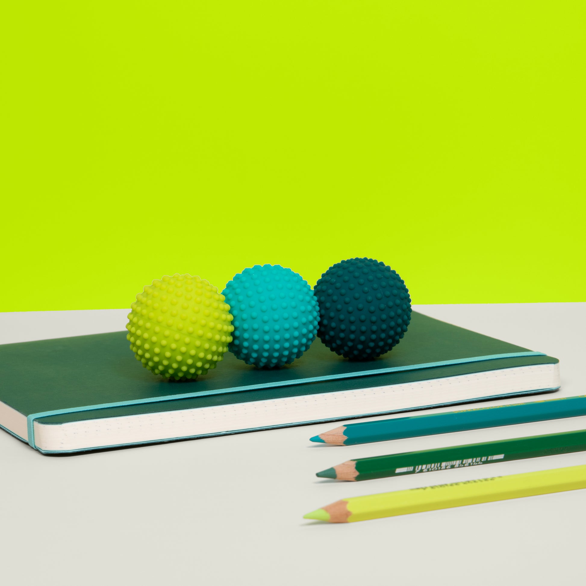 Odds green dots are shown as Three colorful textured balls on a notebook with pencils in front against a green background