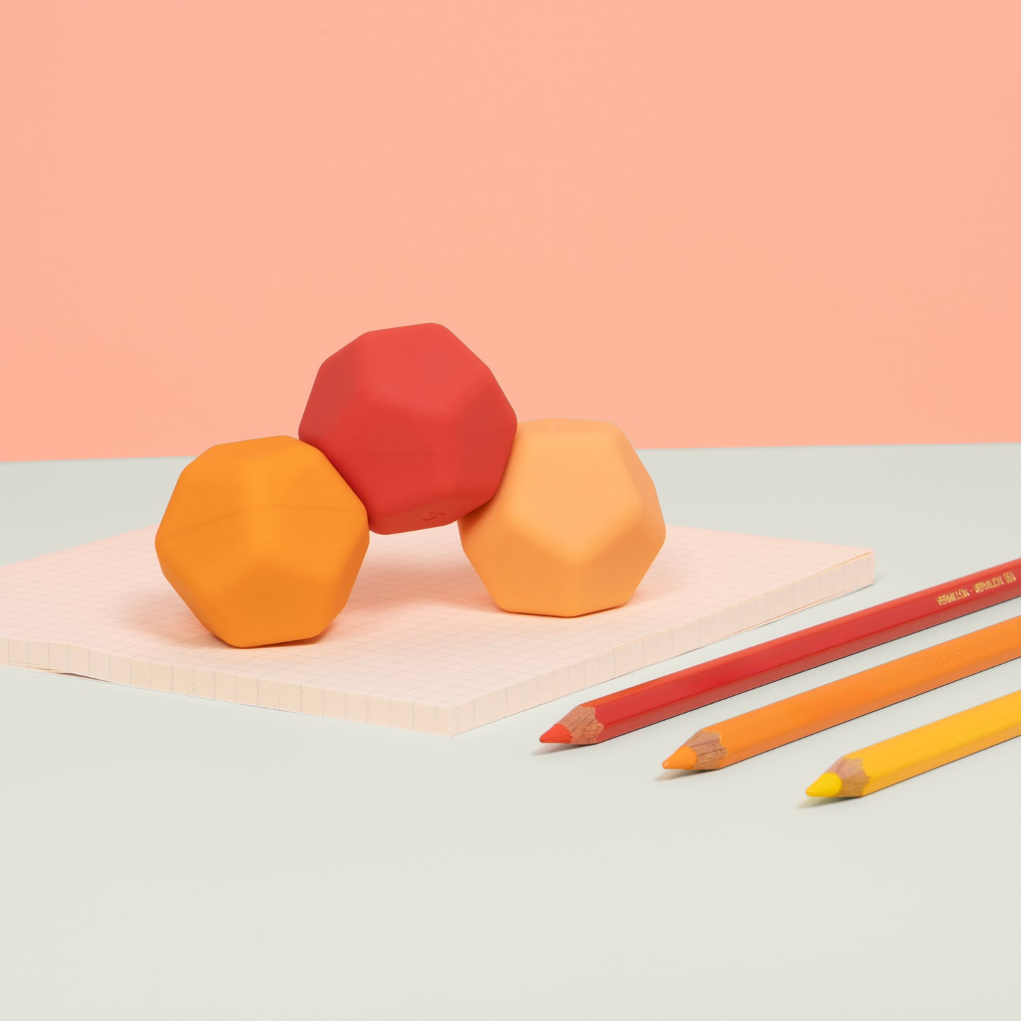 Odds Orange planes with matching stationary. Three colorful clay blocks on a light surface with two pencils nearby, against a pink background