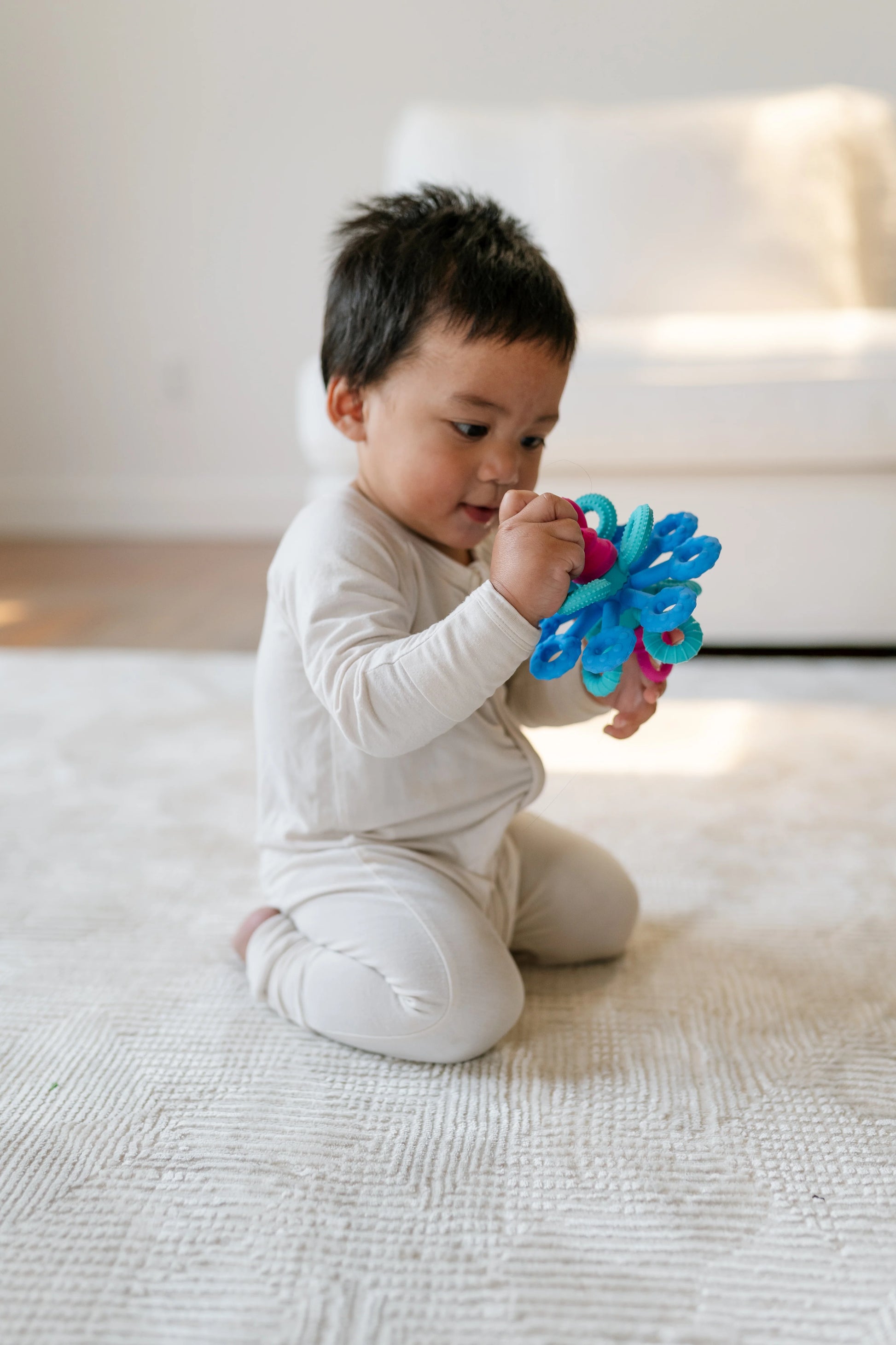 Baby playing with a the okee activity sensory ball toy on a light-colored floor.