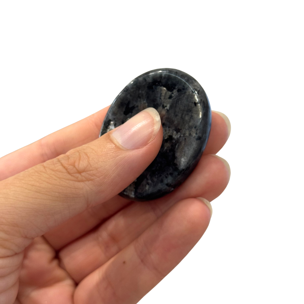 Hand holding a black flash Kaiko Rubbing Stones against a white background