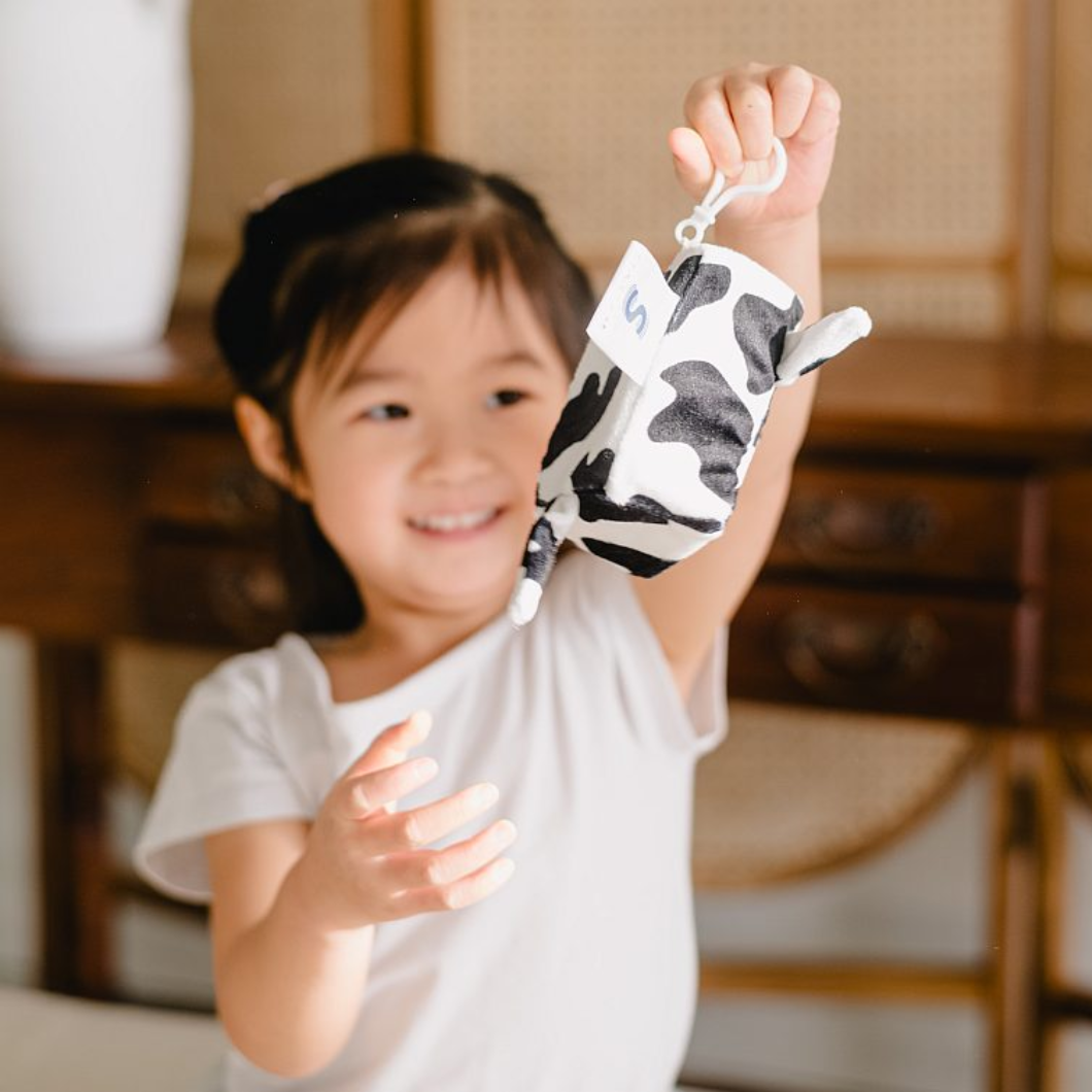 A smiling young girl holding up a cow print vibrating handheld sensory toy.