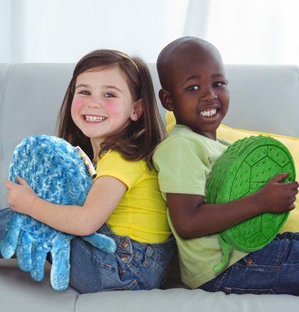 Two children sitting on a couch, each holding a senseez touchables vibrating pillow.