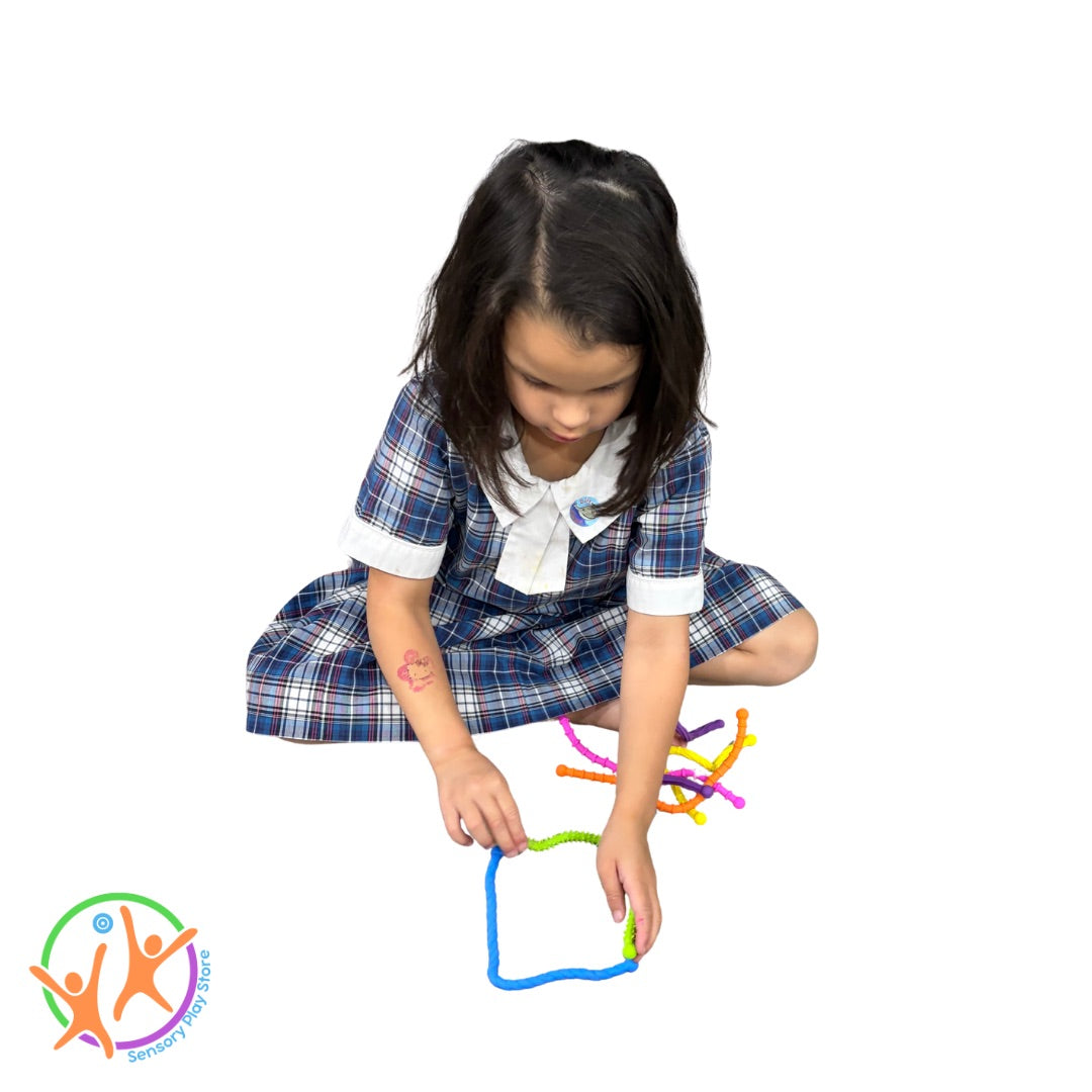 Young girl playing with colourful textured twistable noodle toys on a white background