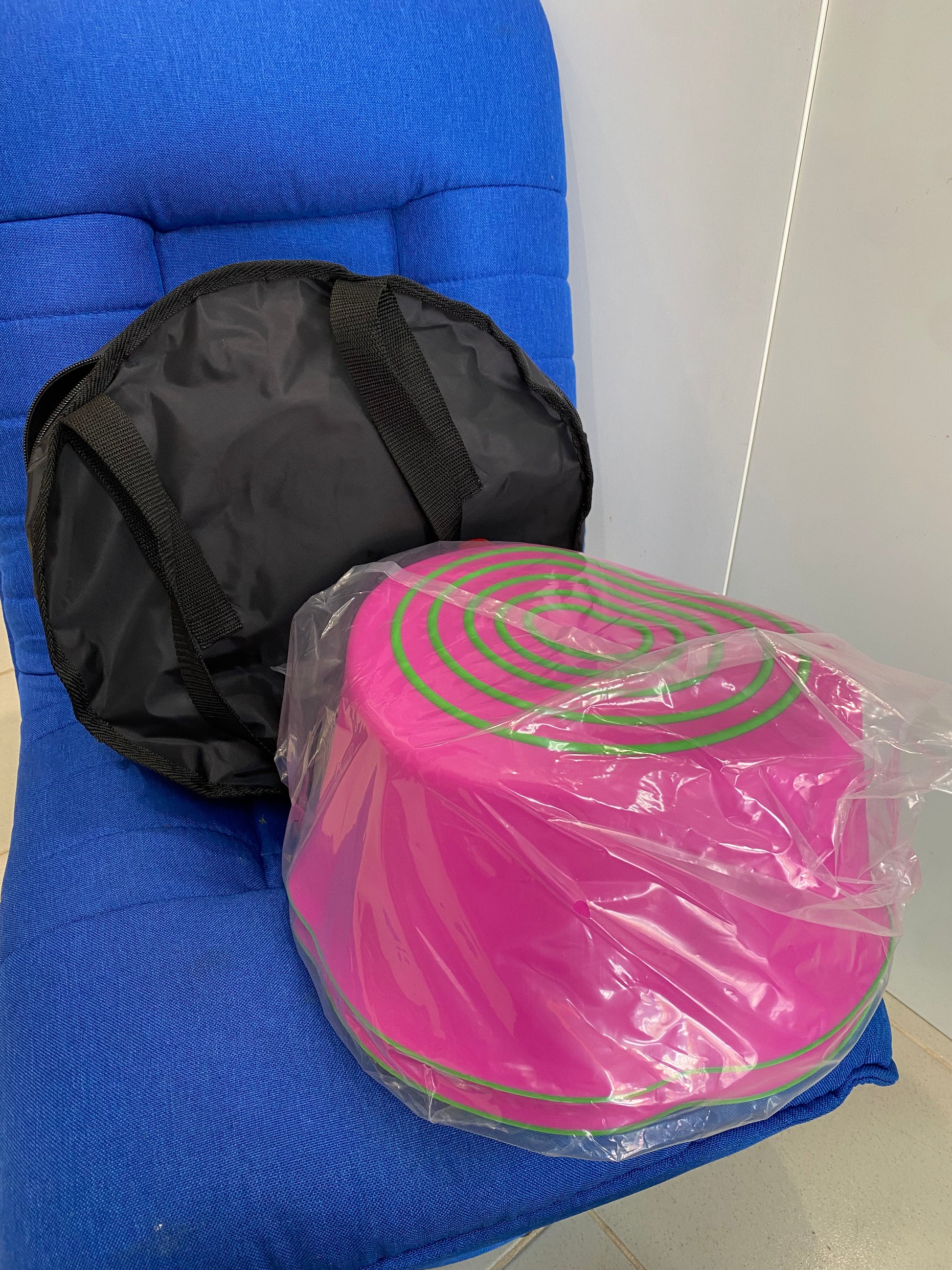 Pink step stool with green stripes in clear plastic wrap on a blue chair.