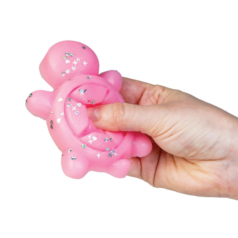 Close-up of a hand squeezing a pink Sticky Fidget Turtle toy, showing its squishy texture and glittery shell.