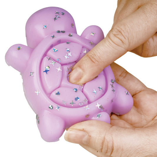 Close-up of a hand squeezing a purple Sticky Fidget Turtle toy, showing its squishy texture and glittery shell.