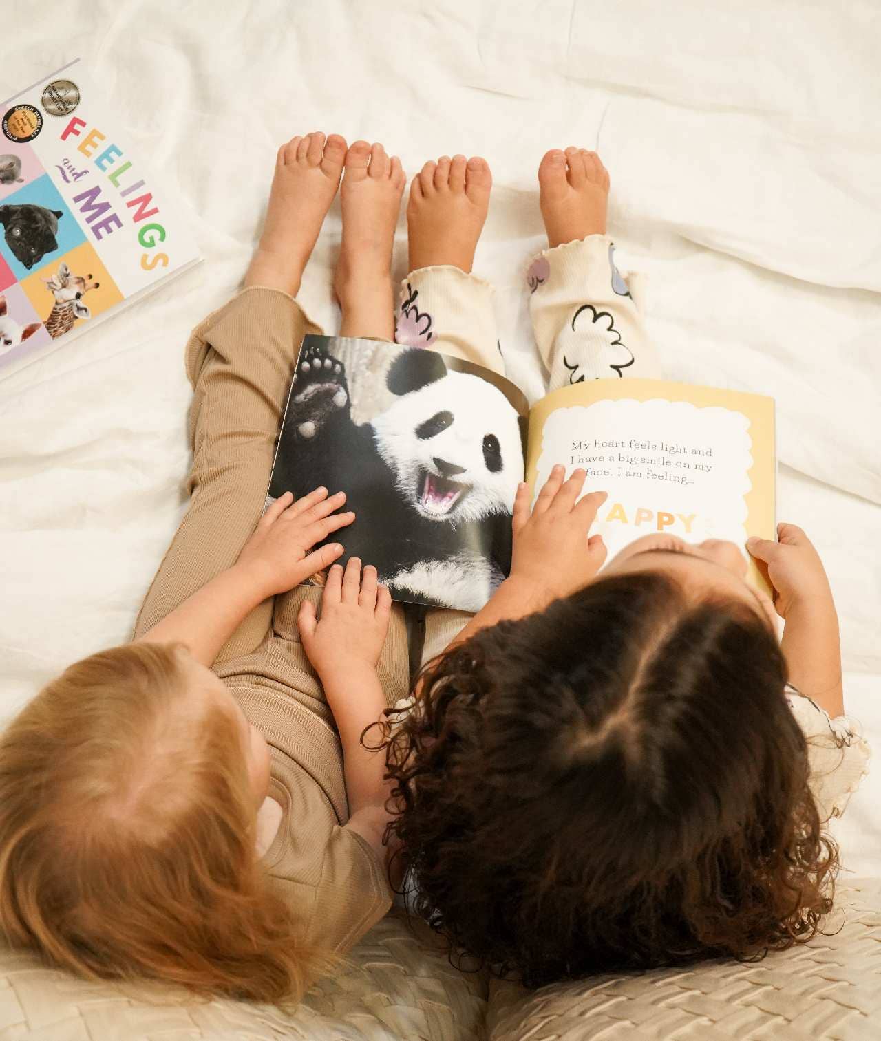 Two children sitting on a bed reading books about feelings with a happy panda.