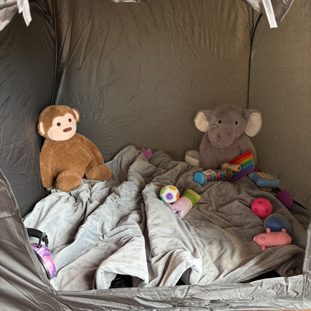 Two stuffed animals in a sensory tent with blankets and toys on a gray background