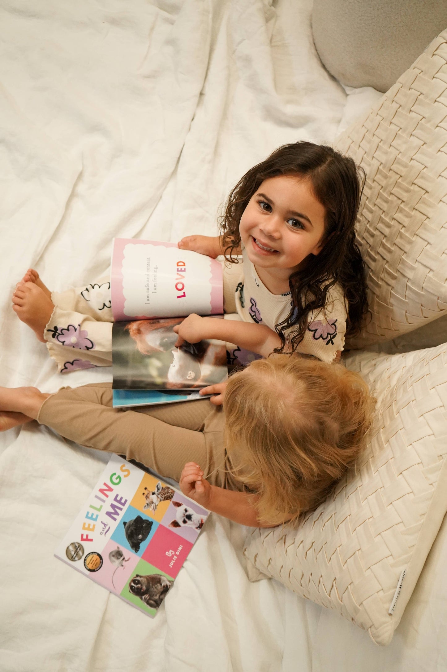 Two children sitting on a bed with books, reading the page 'LOVED'.