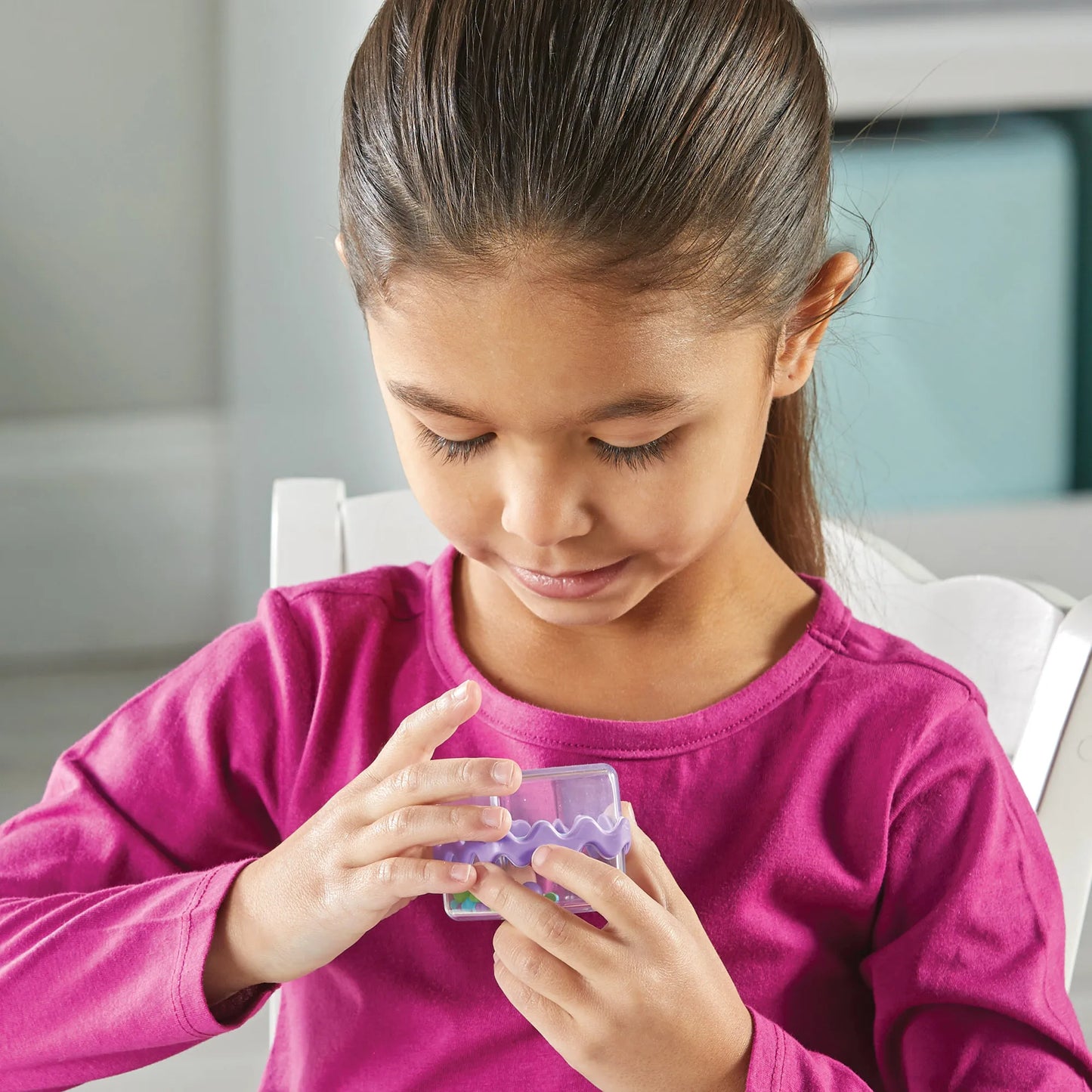 Young girl in a pink shirt holding a small cool down fidget cube 