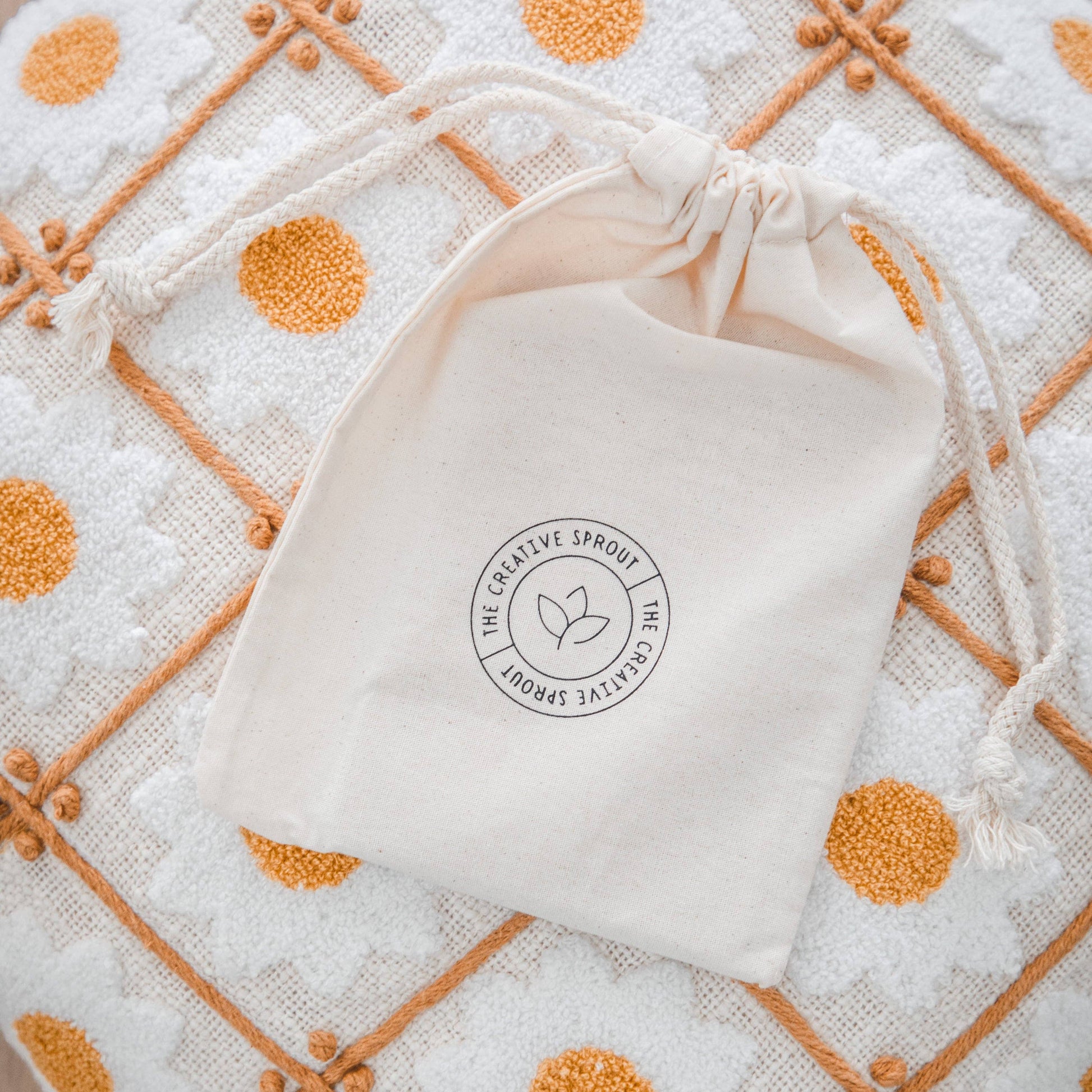 White drawstring bag with The Creative Sprout  brand logo on a patterned fabric background