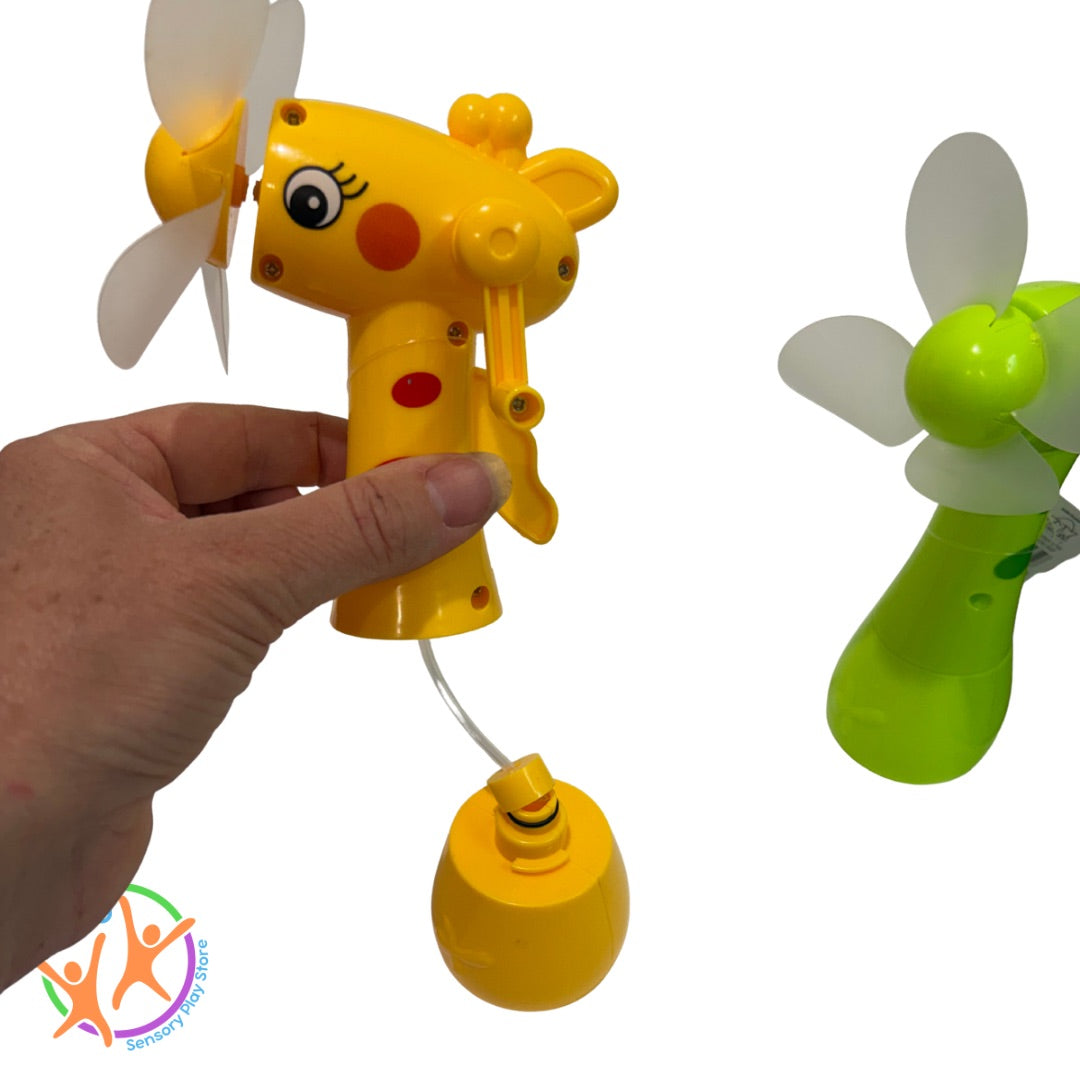 Yellow toy mist fan opened and  held by a hand, next to a green misting fan on a white background.