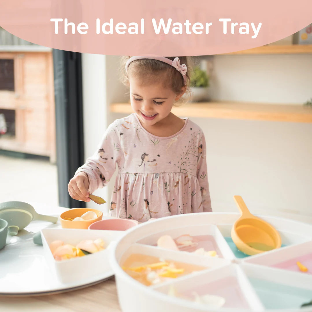 Child playing with a water in a sensory play tray in a kitchen setting.