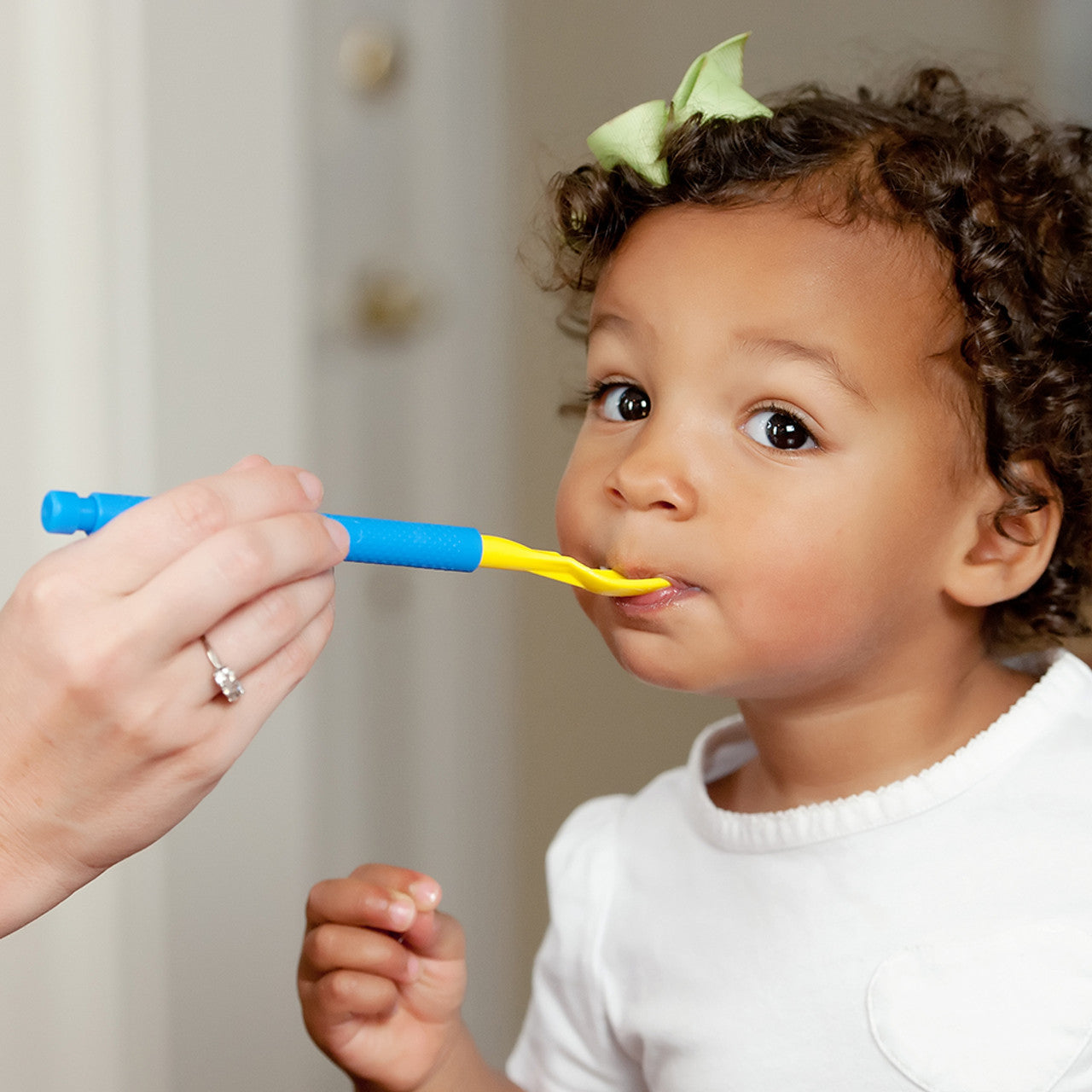 Child being fed by an adult using the  yellow spoon tip attached to the ARK z Vibe